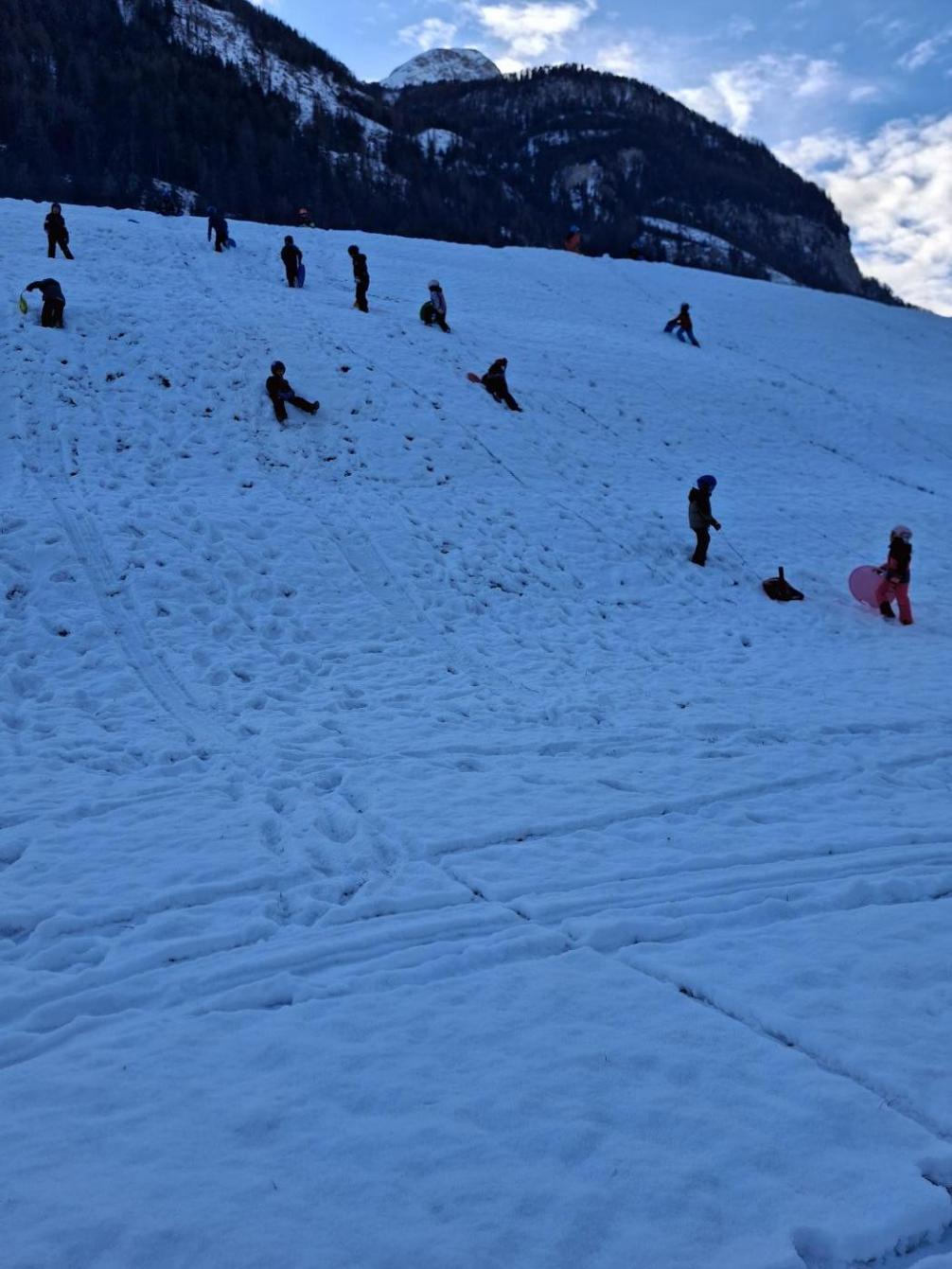 Kinder rutschen auf Rutschtellern einen Hang hinunter