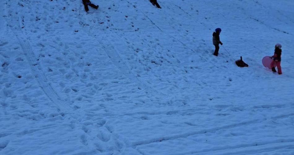 Kinder rutschen auf Rutschtellern einen Hang hinunter